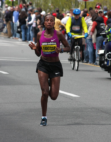Competitor Teyba Erkesso in the Boston Marathon. She is a Black woman wearing athletic shorts and a tank top and is near the end of the course, sweating heavily.