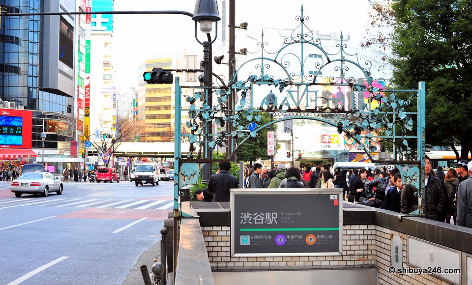 A different angle looking at Shibuya over the subway sign towards the Scramble Crossing.