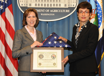 FFAS Deputy Under Secretary Darci Vetter (left) accepts the flag  from Ambassador Haslach (right).