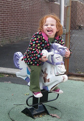 little girl in colorful dotted coat makes a wild face on hobby horseback