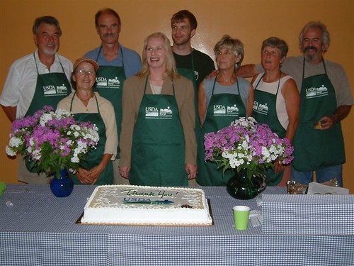 USDA Rural Development State Director Virginia Manuel (center) poses with contributors to the project.  Paula Day, the President of Maine Alternative Agriculture Association presented a cake thanking USDA Rural Development for their support and funding.  Pictured from left to right wearing presented by USDA are:  Ed Ross, Arlene Walker, Ernie Hilton, Virginia Manuel, Ian Baxter, Paula Day, Kathie Duncan, and Pat Manley, the mason who built the oven.