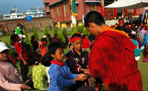 Tibetan children being given nectar from the Hevajra initiation by a monk, Tharlam Monastery courtyard, Boudha, Kathmandu, Nepal by Wonderlane