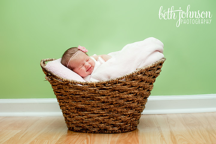 baby girl in basket in front of green wall