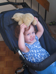 Speck in stroller, grinning, with teddy bear lying on her head
