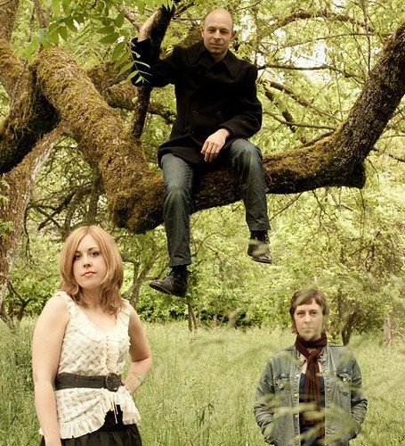 the members of the Corin Tucker Band hang out in a grassy field. The sky is grey.