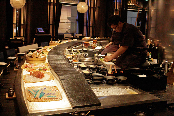 The restaurant's main dining area is a circular ring, and the chefs kneel elevated before the grill