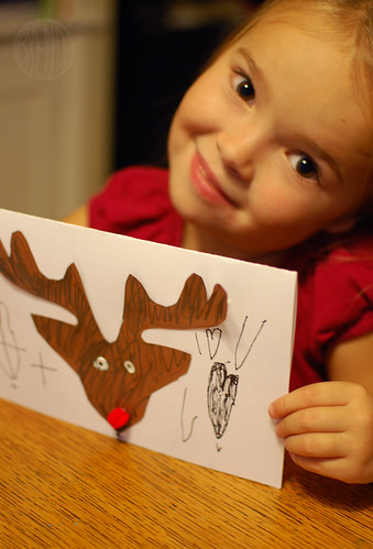 child smiling while holding handmade reindeer Christmas card