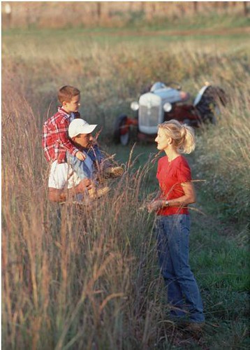 A family stands in a plot of tall grass plantings on a farm in central Iowa. NRCS photo.