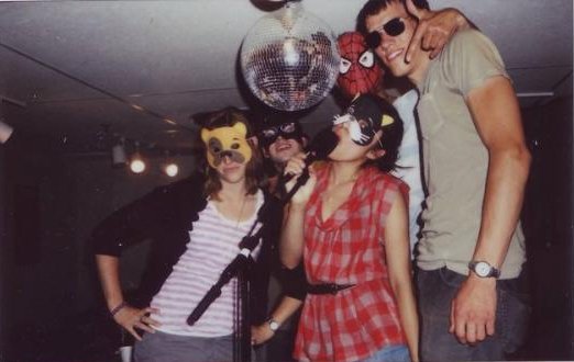 Five young people, including two women, mostly wearing masks, grin candidly under a disco ball into a polaroid camera