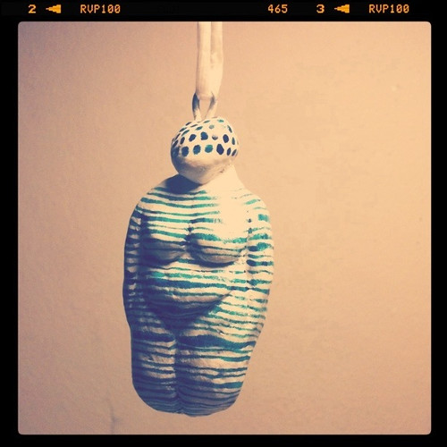 Photo of a fat figurine with no hands or feet, sort of like the Venus de Willendorf, painted white with green horizontal stripes and polka dot hair.