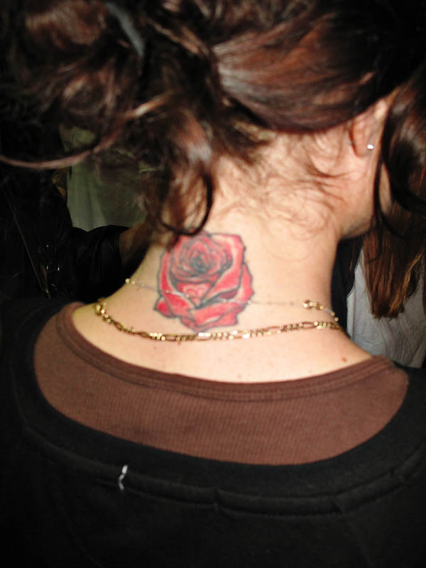 Rose Tattoo on the back of the neck, gold chains, brown top under black top.