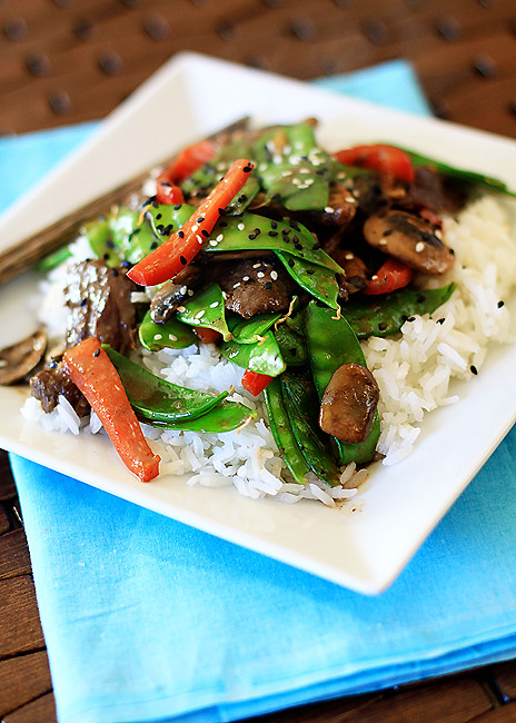 Beef with snow peas stir-fry over rice on a white square plate. 