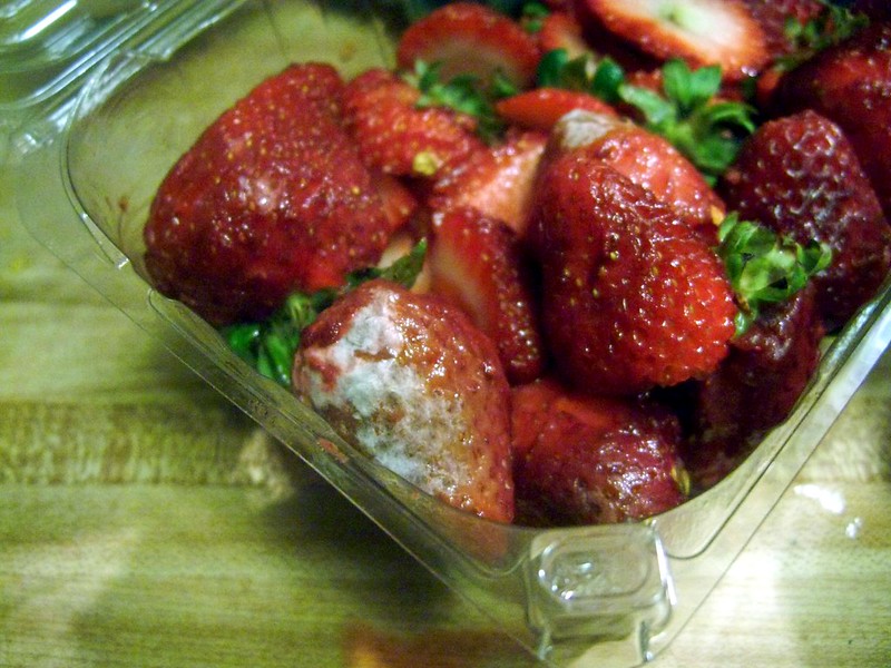 A plastic container with some moldy strawberries