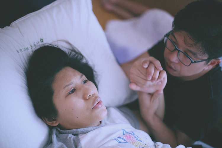 丈夫俯身靠近孕婦，雙手握著她抬起的手。